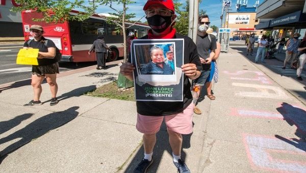 A protester holds a photo of a Mexican informal worker killed by COVID-19. Toronto, Canada. July 28, 2020.
