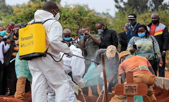 A Kenyan health official (L) wearing a full PPE suite sprays disinfectant on the grave of an identified Covid-19 Coronavirus victim during his burial at a public graveyard in Nairobi, Kenya. August 14, 2020.