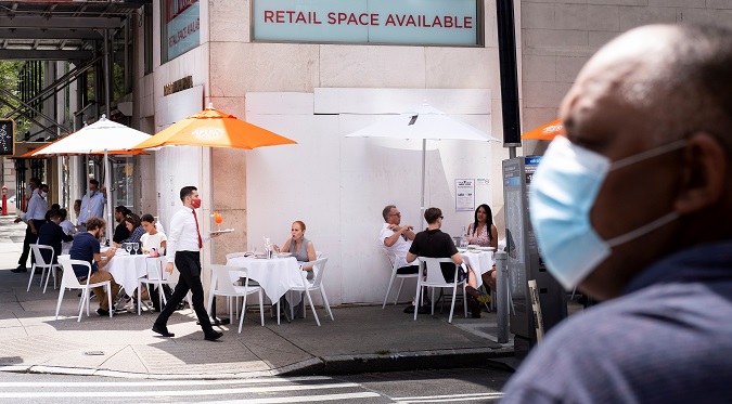 People sit at a restaurant's sidewalk table, set up because indoor dining is still not permitted in the city, in front of a closed designer store on Madison Avenue in New York, New York, USA, 26 August 2020.