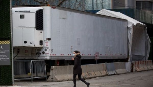 A woman walks past a refrigerated trailer serving as a temporary morgue in New York, the United States, on Jan. 18, 2021.