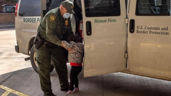 An unaccompanied migrant minor is assisted to board a Border Patrol vehicle by an officer.