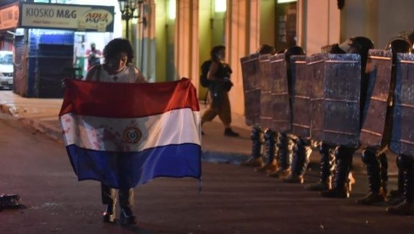 A woman walks with a flag on a street guarded by police officers, Asuncion, Paraguay. 