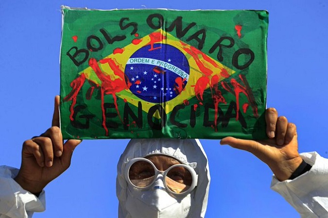 A demonstrator holds an image of the Brazilian flag covered in fake blood and the phrase 
