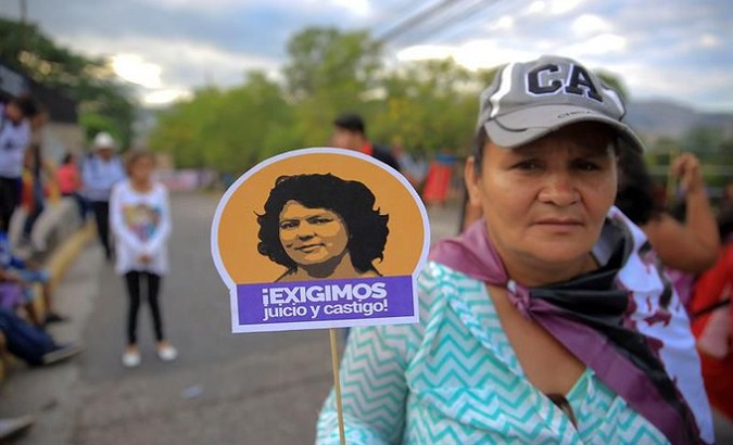 Woman holds a photo of Berta Caceres. The caption says, 