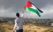 Young man waves a Palestinian flag in front of the territories occupied by Israeli forces.