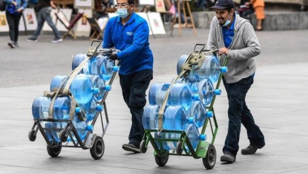 Two men push handcarts stacked with water jugs along a street in Santiago, Chile's capital, on Jan. 17, 2022.