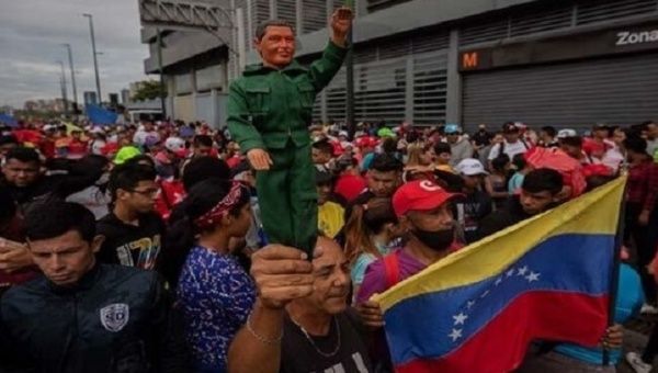 A man holds a Comandante Hugo Chavez doll.