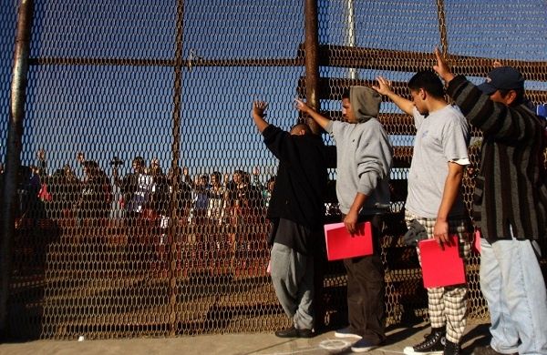 A group of recently deported immigrants stand near the double steel fence that separates San Diego and Tijuana at the border in Tijuana. Photo: Reuters